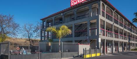Un edificio de varios pisos con un llamativo letrero de Red Roof, que cuenta con balcones y una entrada con portón.