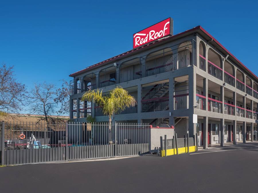 A multi-story building with a prominent Red Roof sign, featuring balconies and a gated entrance.