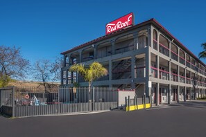 Um edifício com vários andares, com uma placa Red Roof em destaque, varandas e entrada fechada por portão.
