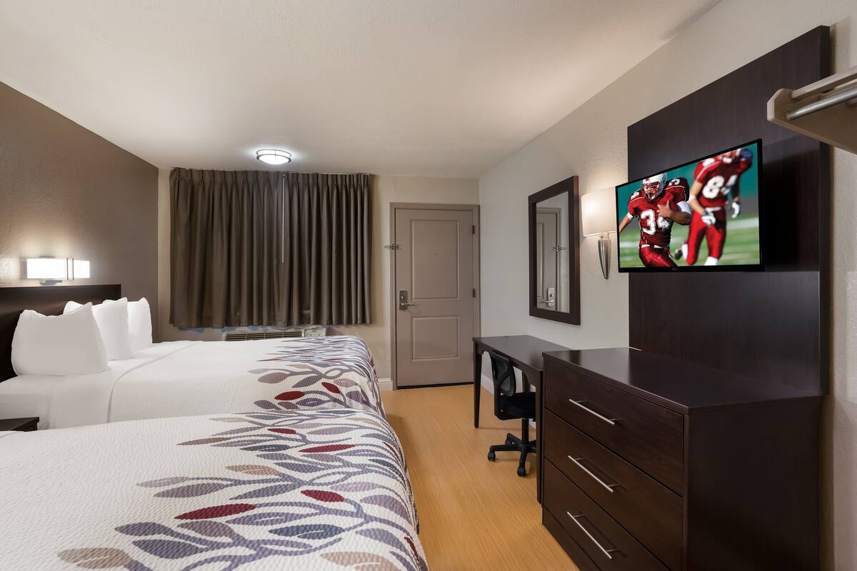A hotel room with two beds, a desk, a TV, and a wardrobe.