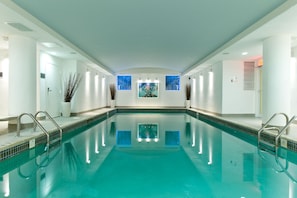 A large indoor swimming pool with clear blue water, surrounded by white walls and a tiled floor.