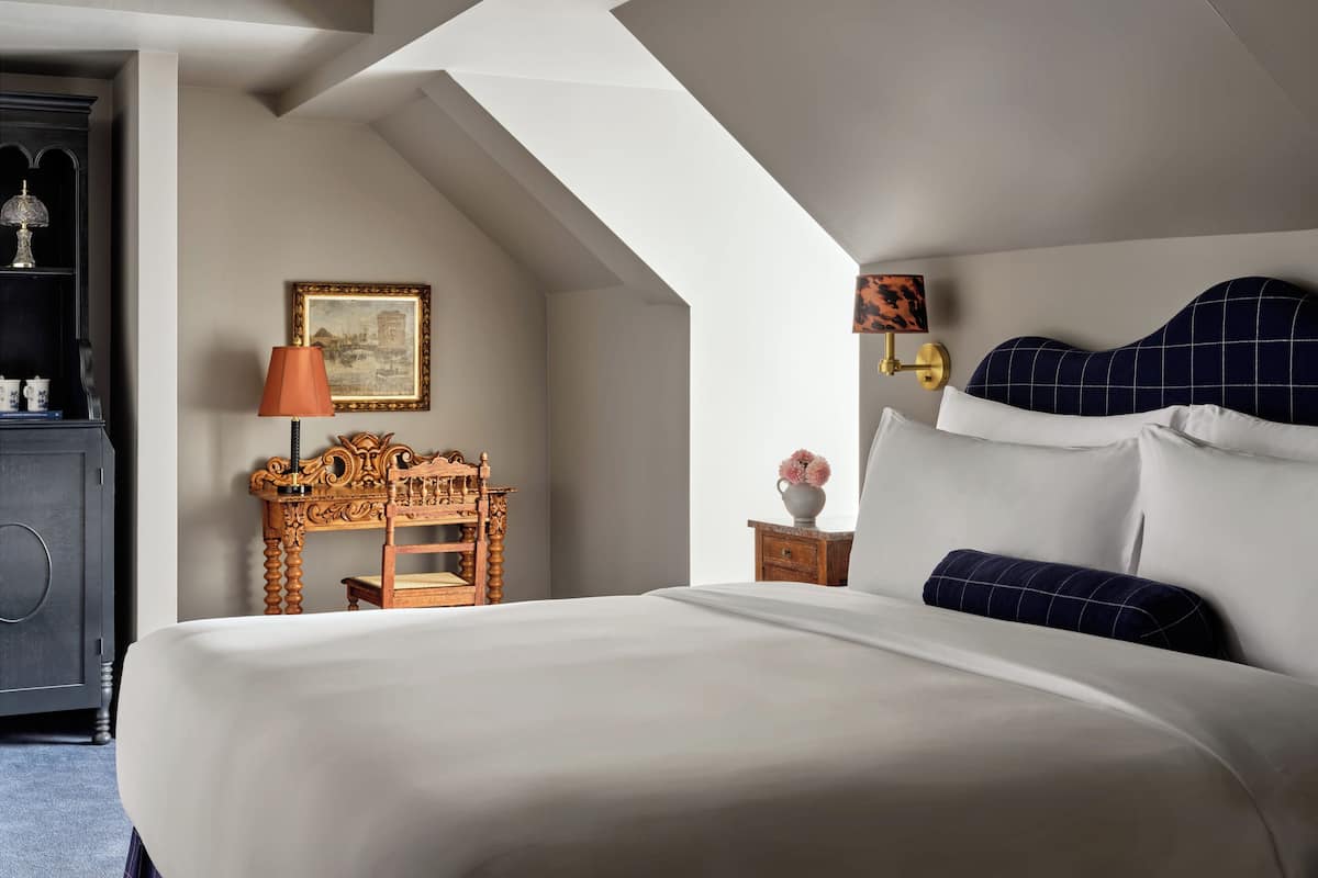 A bedroom with a large bed, a wooden nightstand, a lamp, a framed picture, and a dresser.