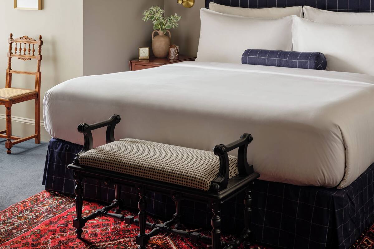 A neatly arranged bedroom with a large bed, a chair, a small table with a plant, and a wall-mounted lamp.