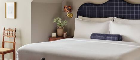 A neatly arranged bedroom with a large bed, a chair, a small table with a plant, and a wall-mounted lamp.