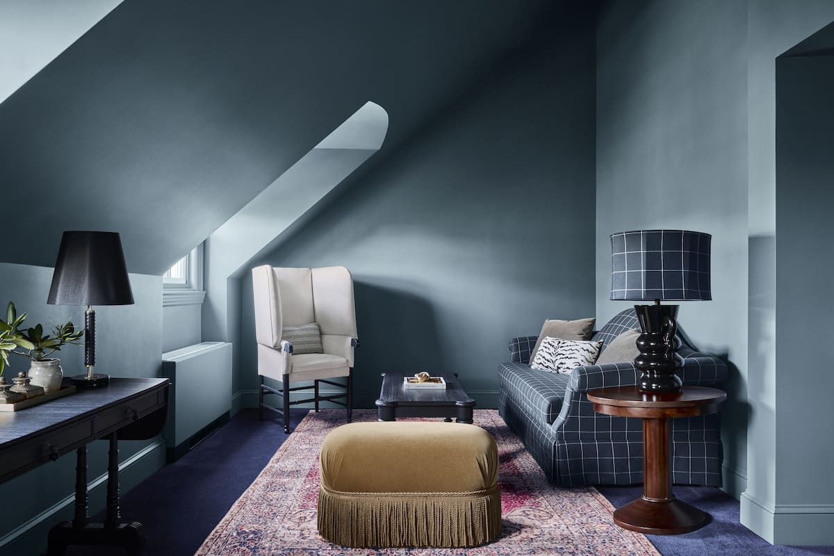 A cozy loft bedroom with a high ceiling, a sofa, a chair, a small table, and a lamp.