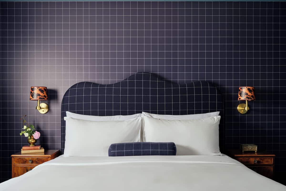 A neatly made bed with white linens, a dark headboard, and two bedside tables with lamps.