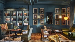 A room with dark blue walls, wooden furniture, and framed portraits on the wall. - The Vanderbilt, Auberge Collection (Newport)