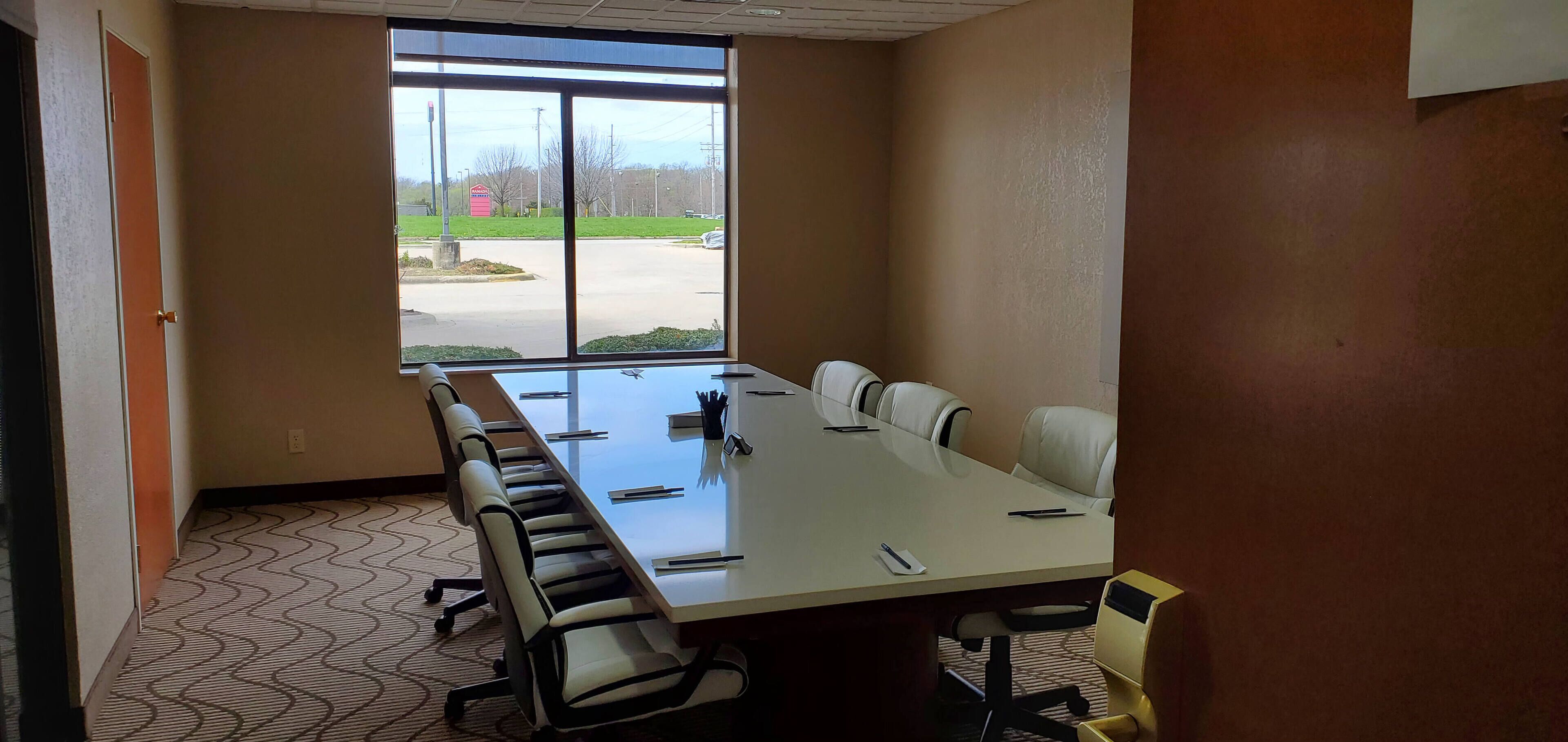 A conference room with a long table, chairs, and a view of a parking lot through large windows.