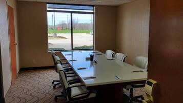 A conference room with a long table, chairs, and a view of a parking lot through large windows.
