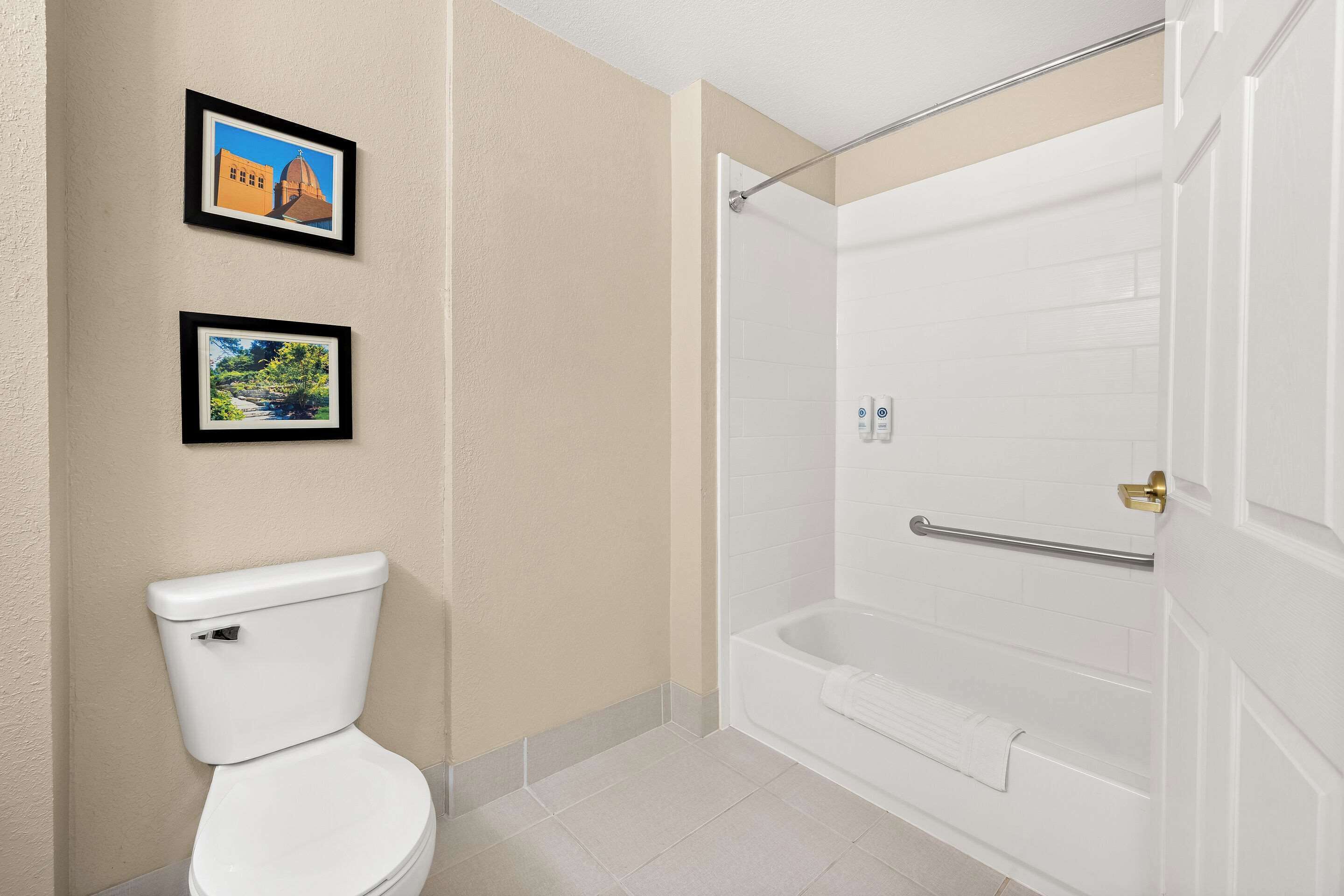 A bathroom with a toilet, a framed picture of a building, and a walk-in shower.