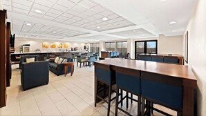 A spacious hotel lobby with a modern kitchen area, comfortable seating, and a bar.