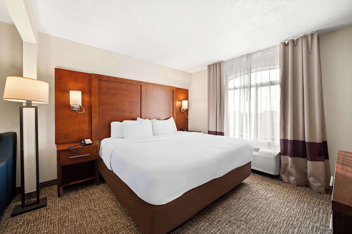 A hotel room with a large bed, a wooden headboard, bedside lamps, a desk, and a chair.