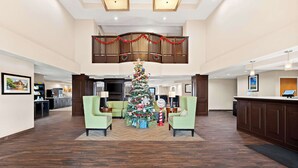 A spacious lobby with a large Christmas tree, green armchairs, and a high ceiling with a decorative railing.