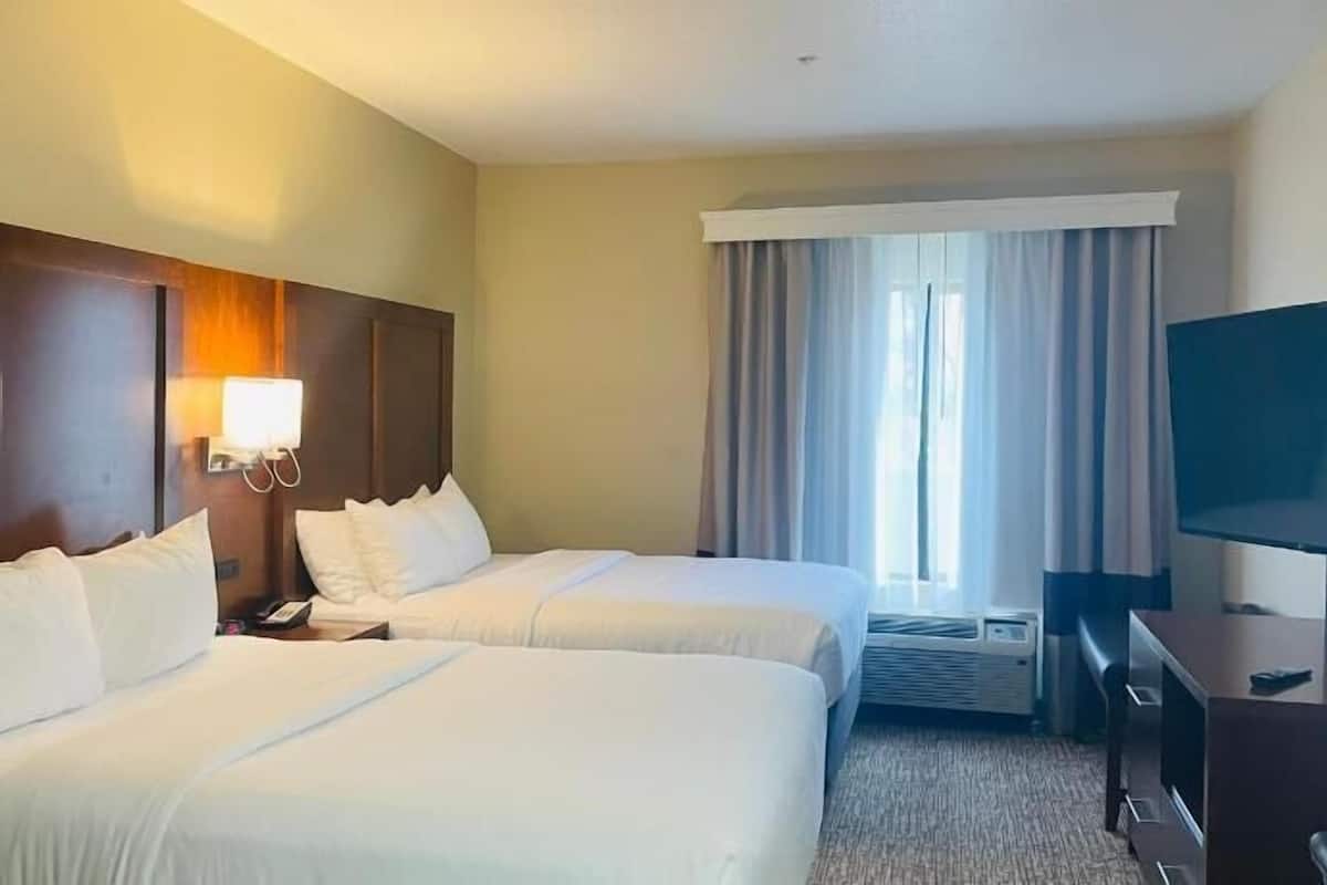 A hotel room with two beds, a desk, a TV, and a window with curtains.