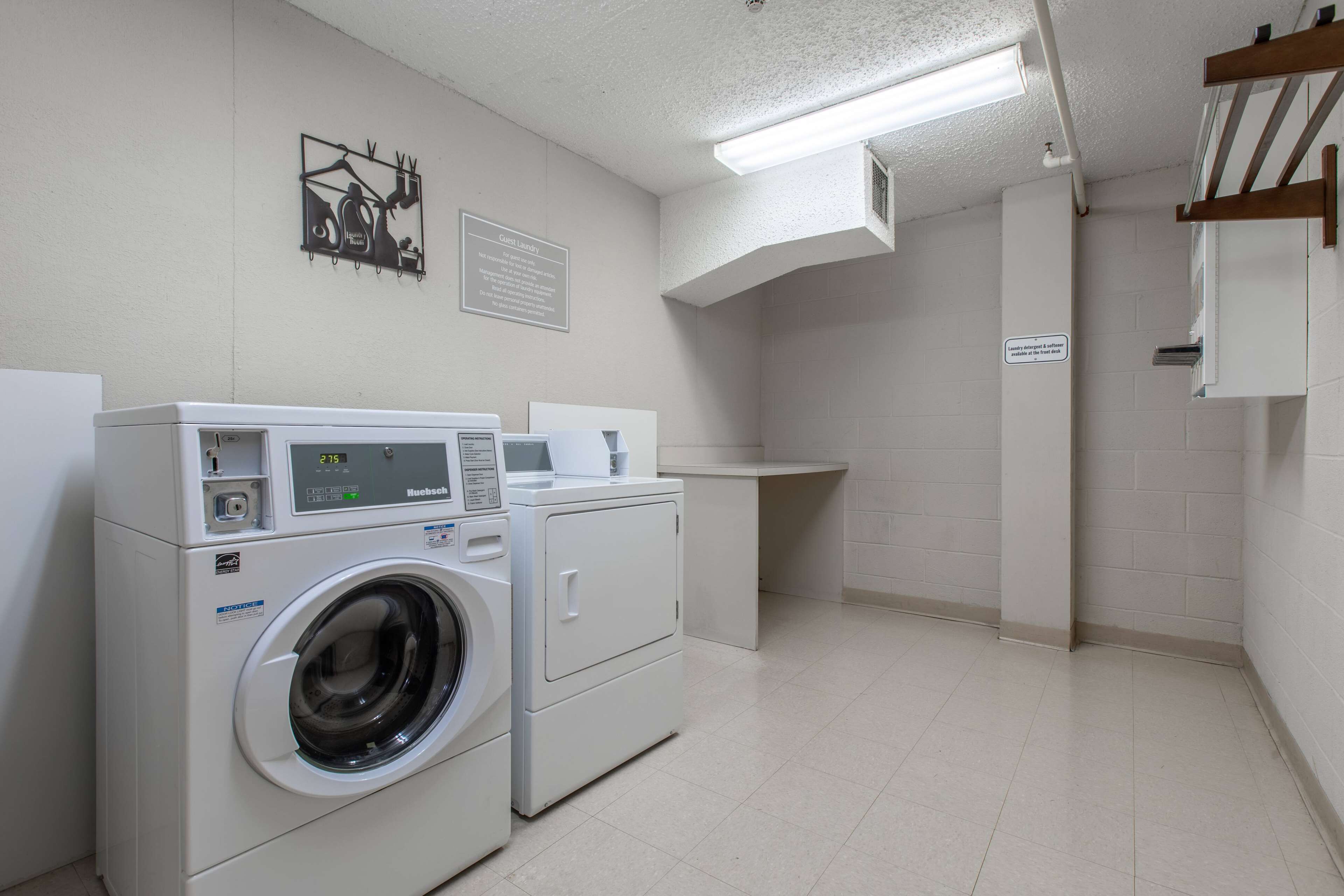 Un espace buanderie comprenant un lave-linge et un sèche-linge à chargement frontal, une petite table avec une tasse et un panneau accroché au mur.