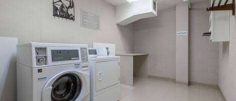 Un espace buanderie comprenant un lave-linge et un sèche-linge à chargement frontal, une petite table avec une tasse et un panneau accroché au mur.