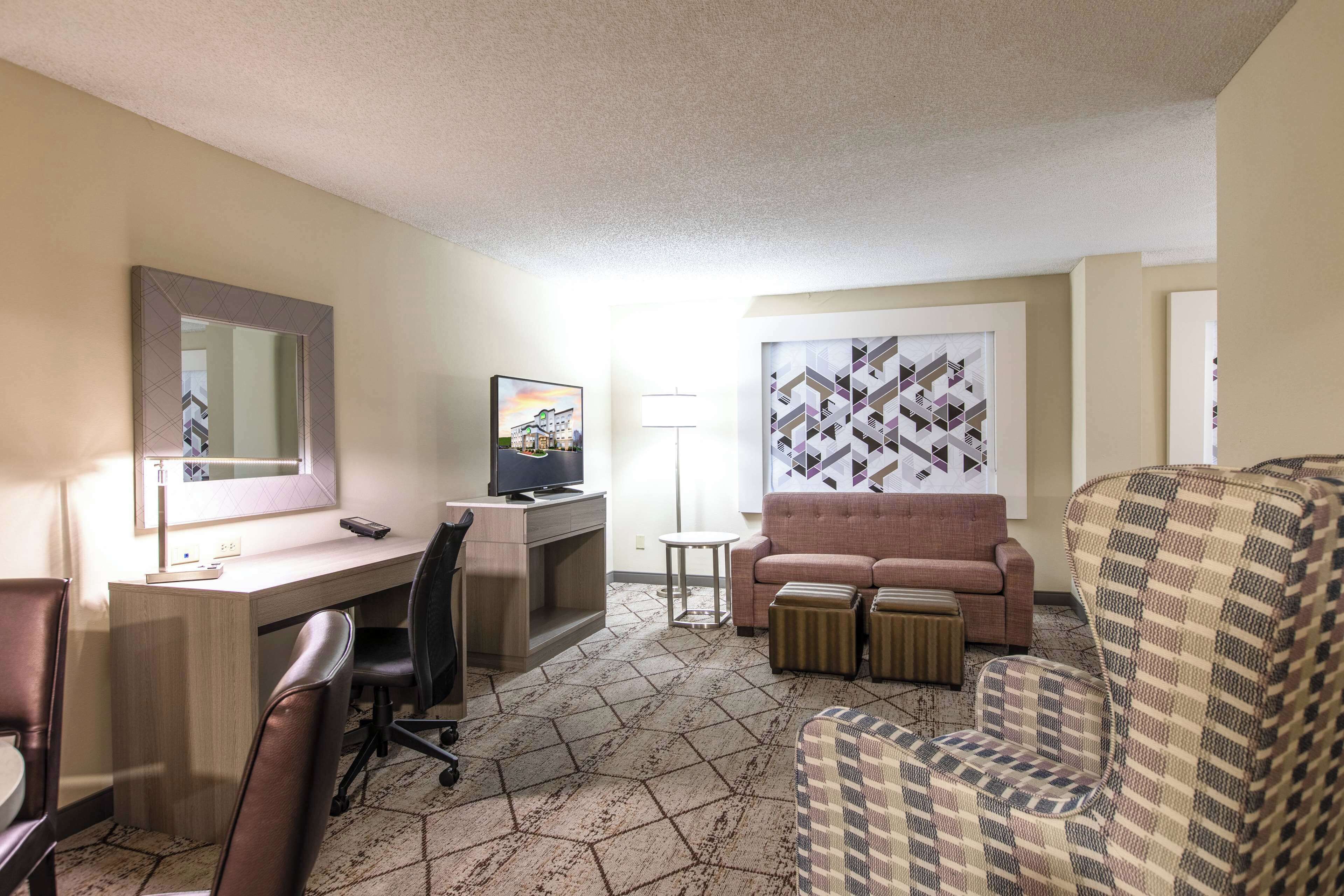 Una habitación de hotel con escritorio, televisor, sofá y un sillón estampado.