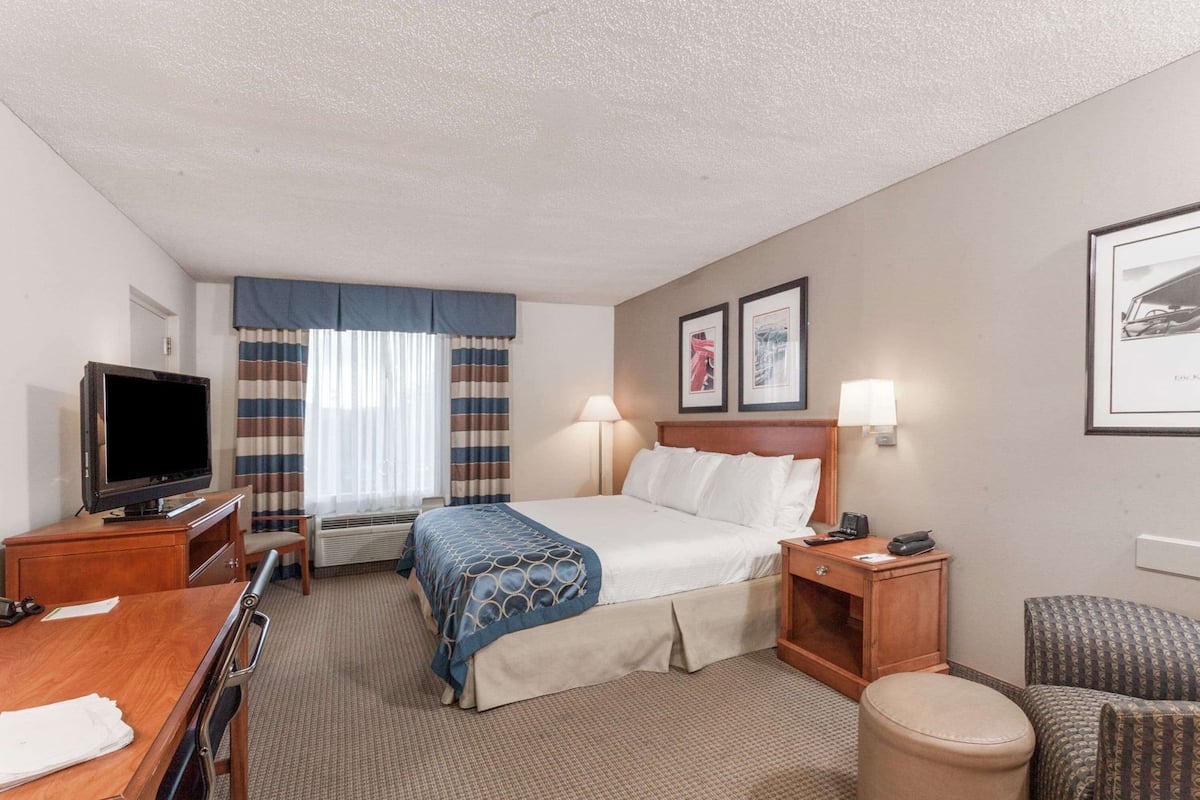 Une chambre d’hôtel comprenant un lit, un bureau avec une télévision, une chaise, une table de chevet et une lampe.