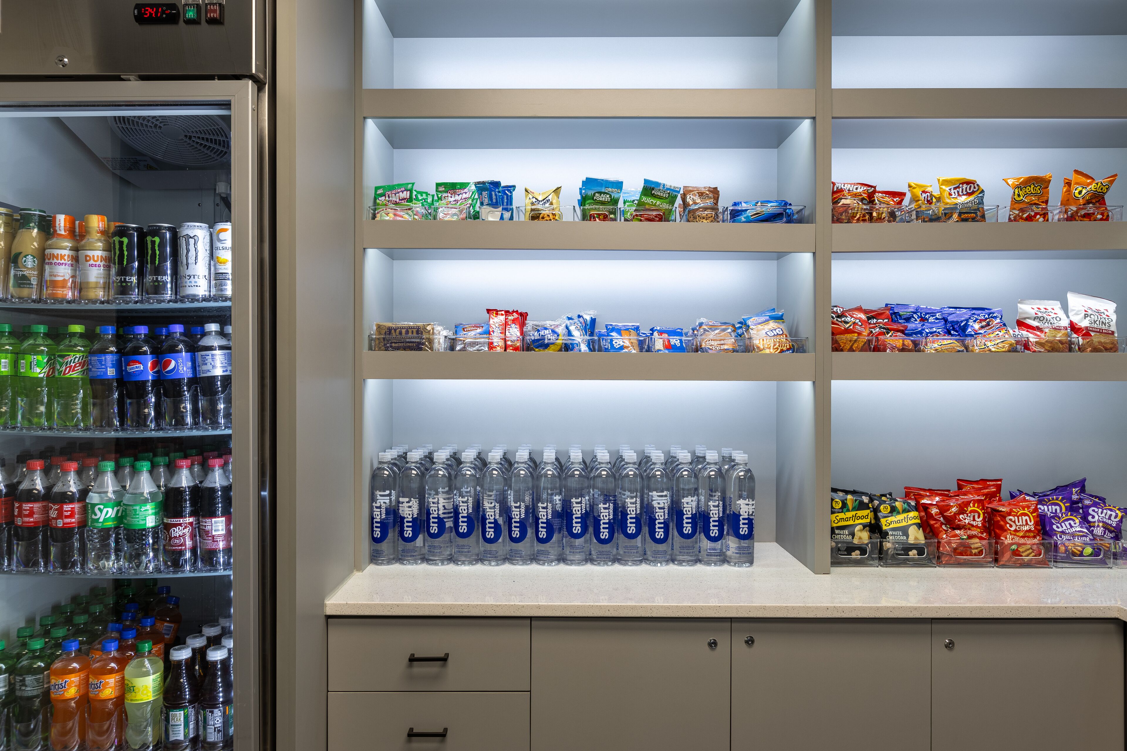 A beverage refrigerator stocked with various drinks and snack shelves containing different brands.