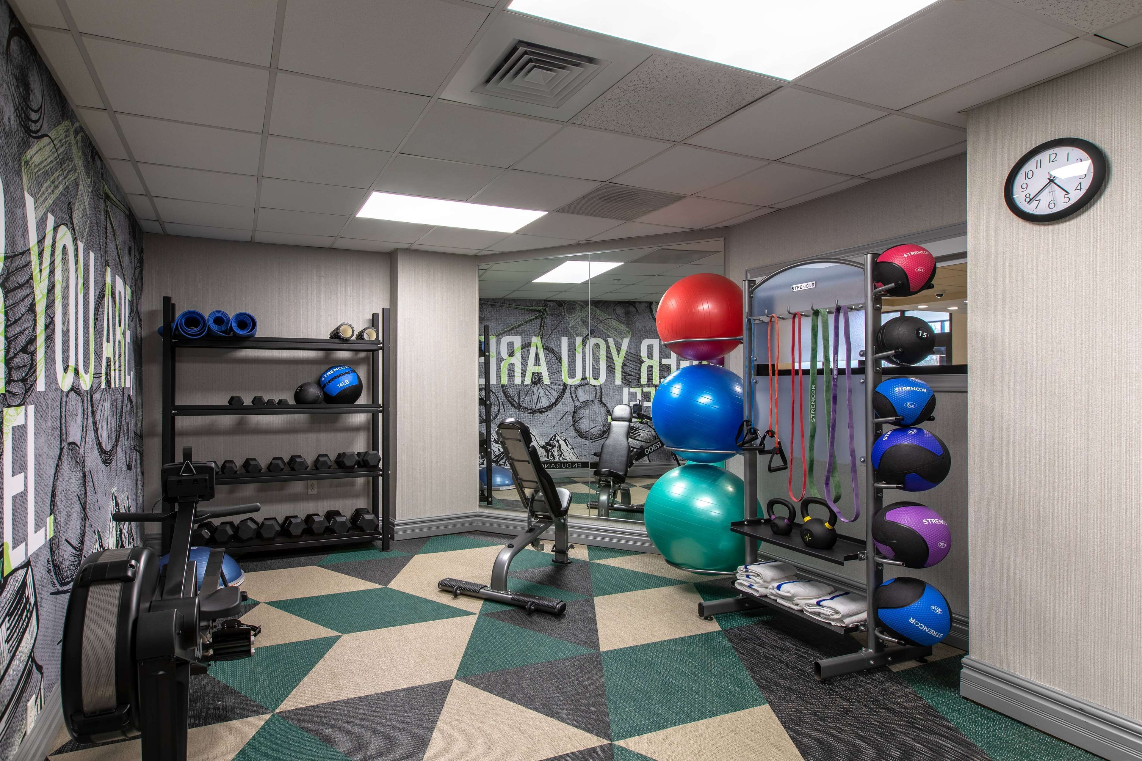 A gym with exercise equipment, a mirror, and a clock on the wall.