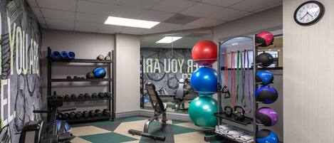 A gym with exercise equipment, a mirror, and a clock on the wall.