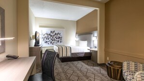 A hotel room with a bed, a desk, a chair, a TV, and a wall with geometric patterns. - Wingate by Wyndham Charlotte Speedway/Concord (Concord)