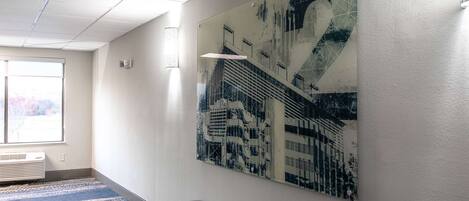 Un couloir orné d’un grand tableau abstrait au mur, avec un banc et une fenêtre équipée de stores.