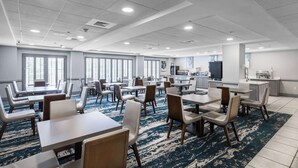 A spacious hotel dining area with multiple tables and chairs, large windows, and a kitchen area in the background. - Wingate by Wyndham Charlotte Speedway/Concord (Concord)