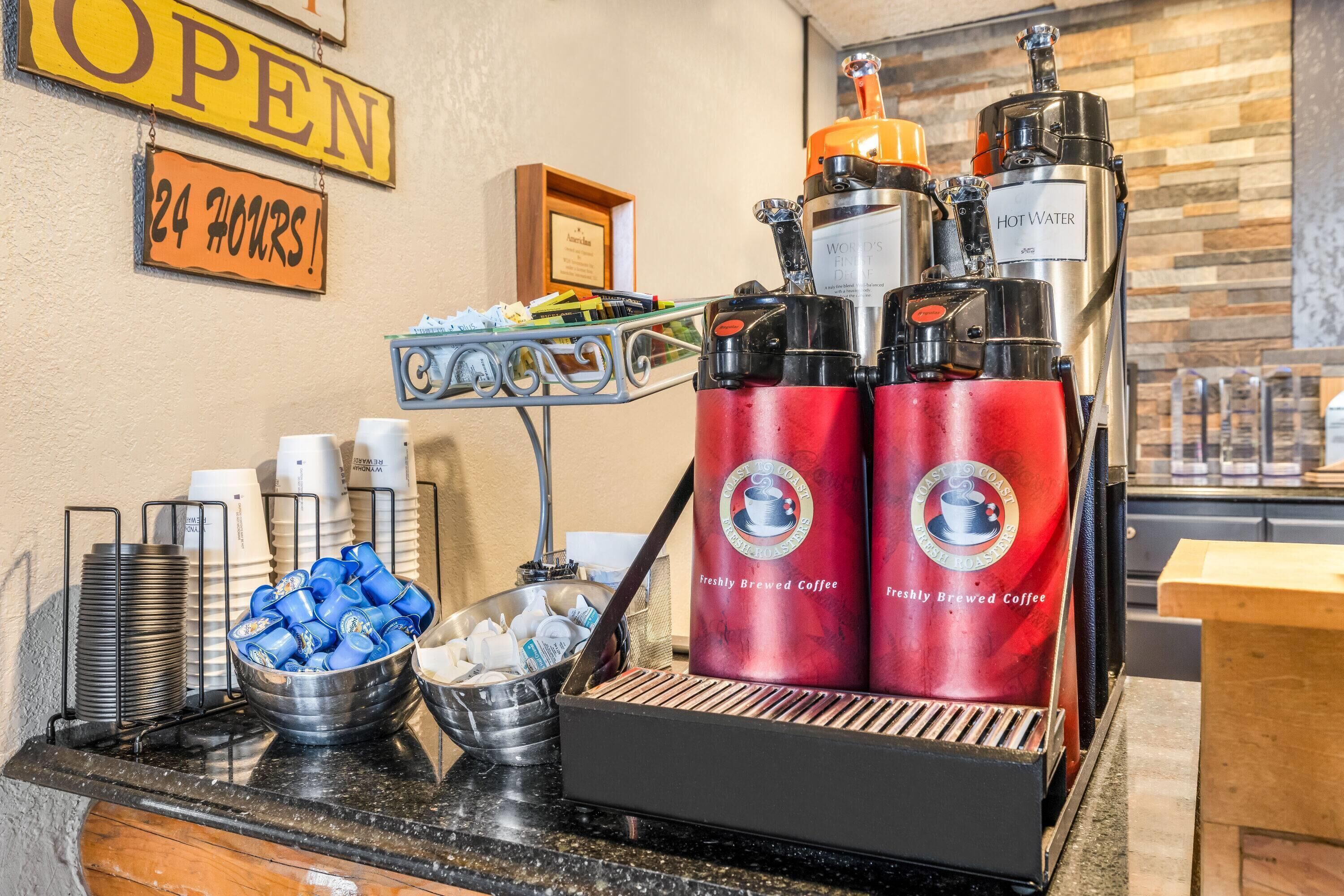 A coffee station with a coffee machine, cups, and a sign indicating 24-hour service.