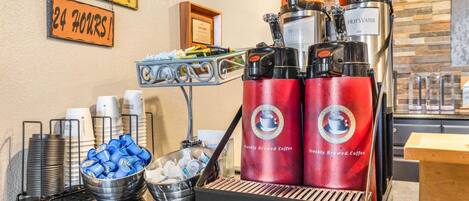 A coffee station with a coffee machine, cups, and a sign indicating 24-hour service.