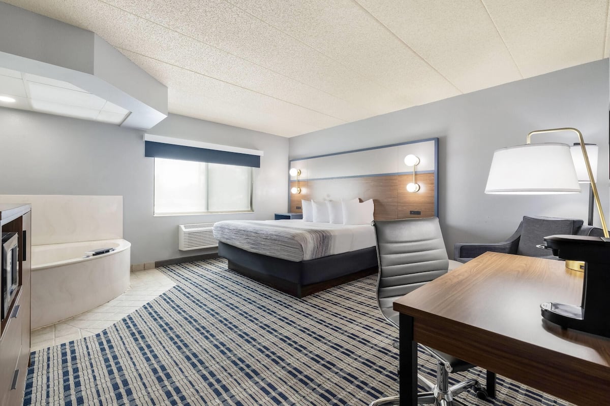A modern hotel room with a bed, a desk, a chair, a vanity, and a large window.