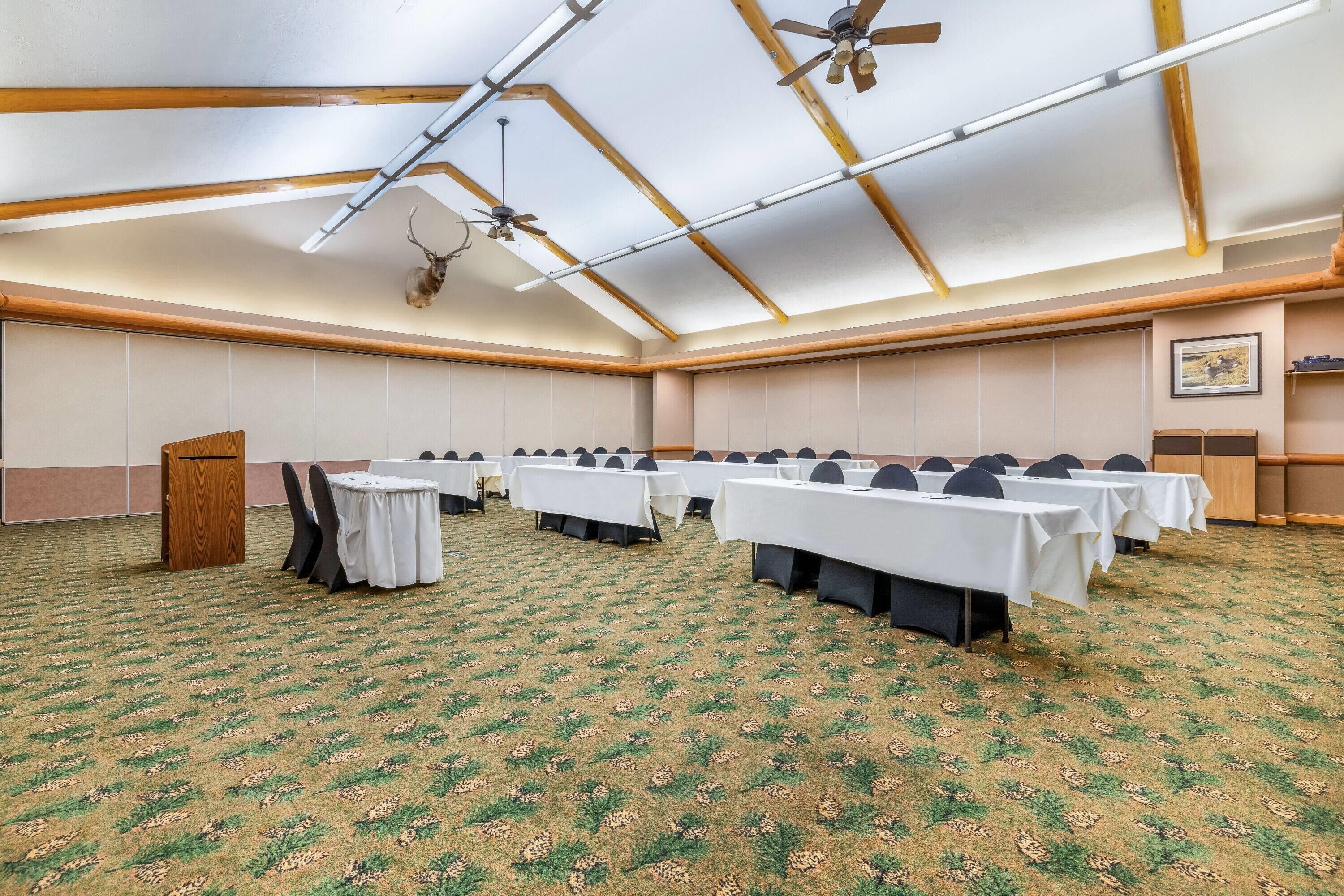 A conference room with tables set up for a meeting, ceiling fans, and a wooden podium.