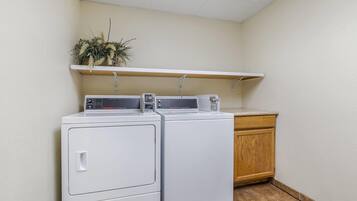 A laundry area with two stacked washers and dryers, a wooden cabinet, and a shelf with plants.
