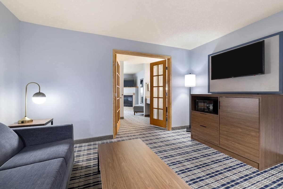 A modern hotel room with a grey sofa, a wooden coffee table, a flat-screen TV, and a wooden cabinet.