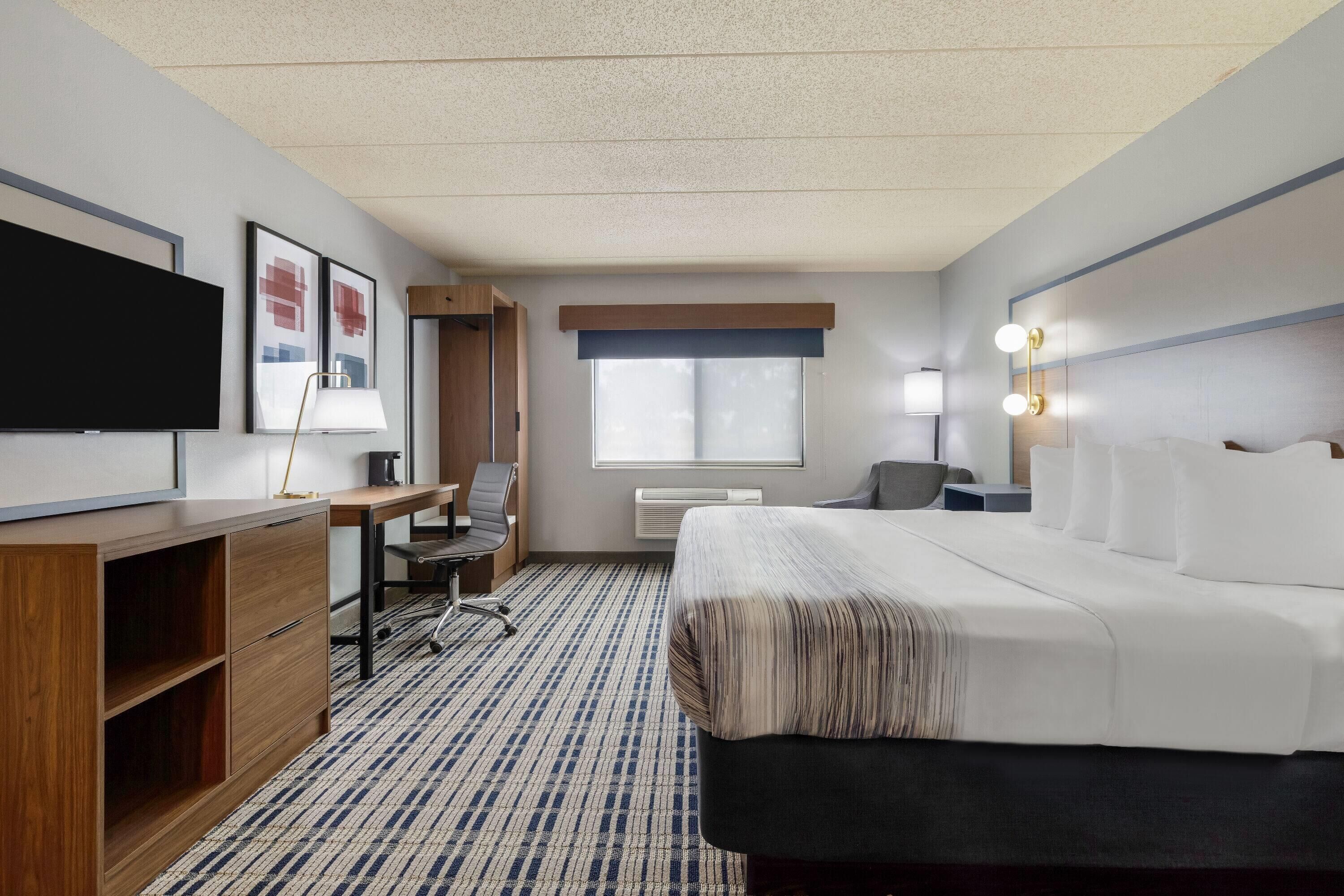 Une chambre d’hôtel équipée d’un lit, d’un bureau, d’une chaise, d’une télévision et d’une fenêtre avec des stores.