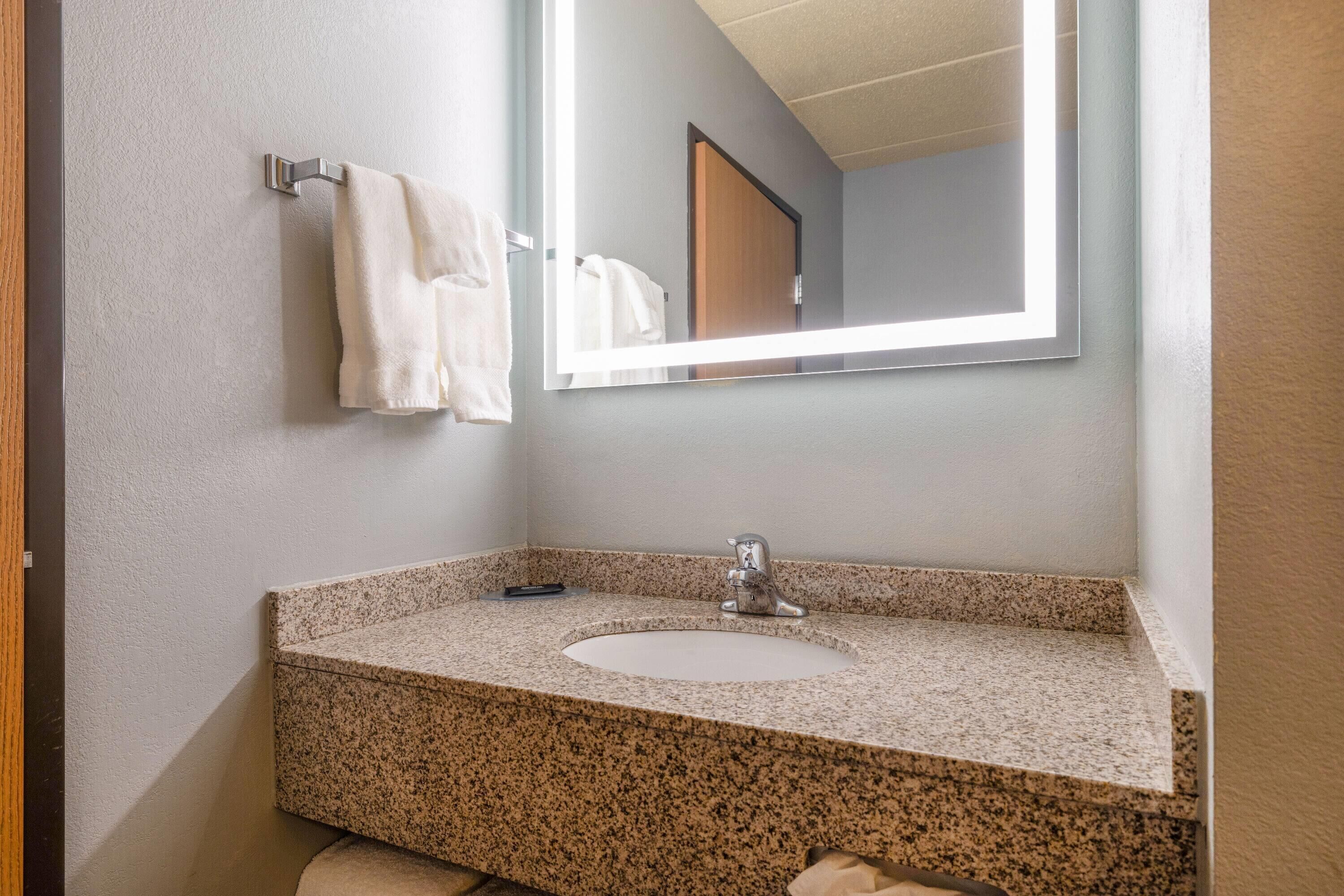 Une salle de bain avec un lavabo doté d’un plan de travail en granit, un miroir et un porte-serviettes.
