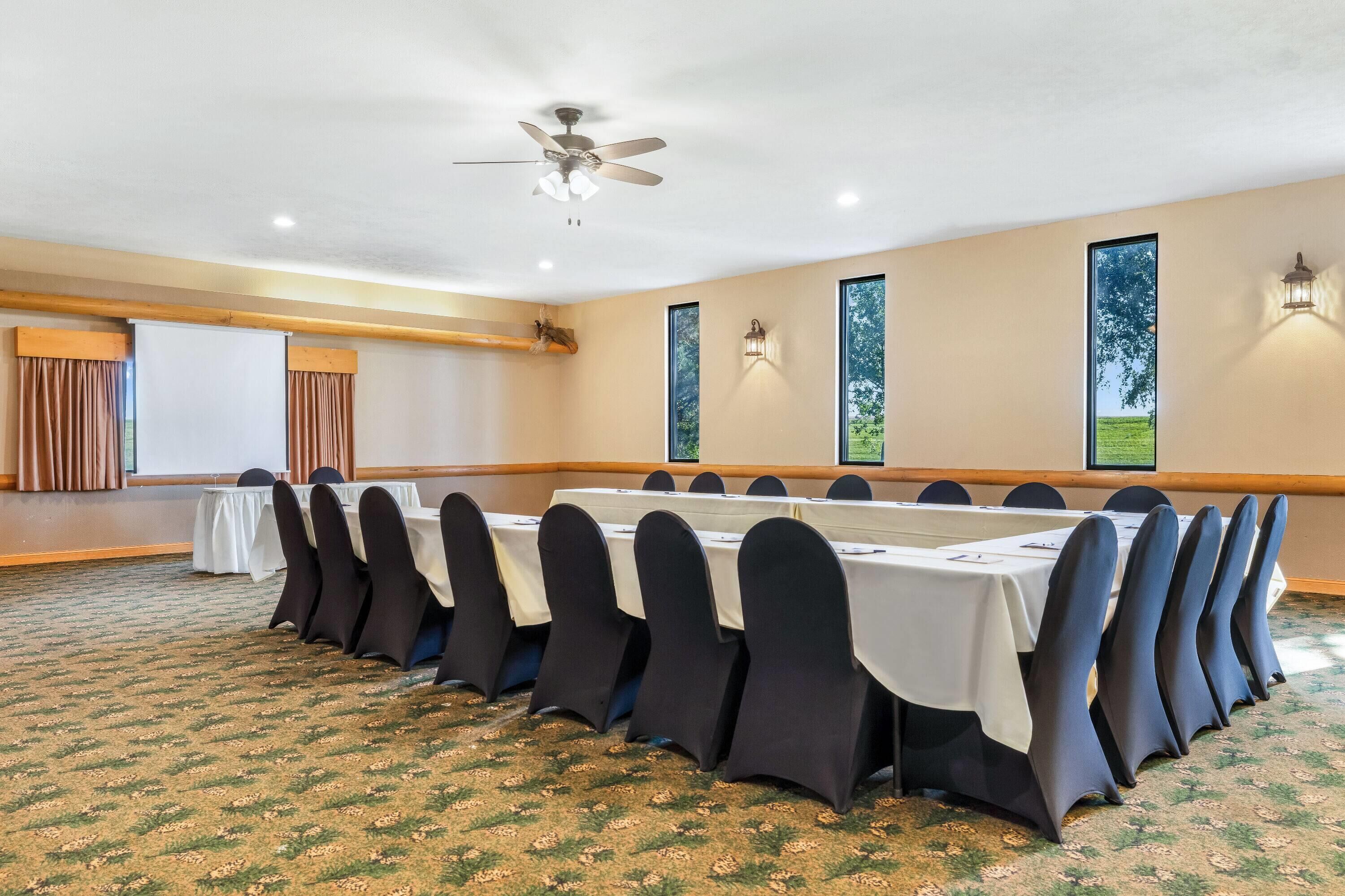 Un salón de conferencias con una larga mesa, sillas negras, paredes color beige y un ventilador de techo.