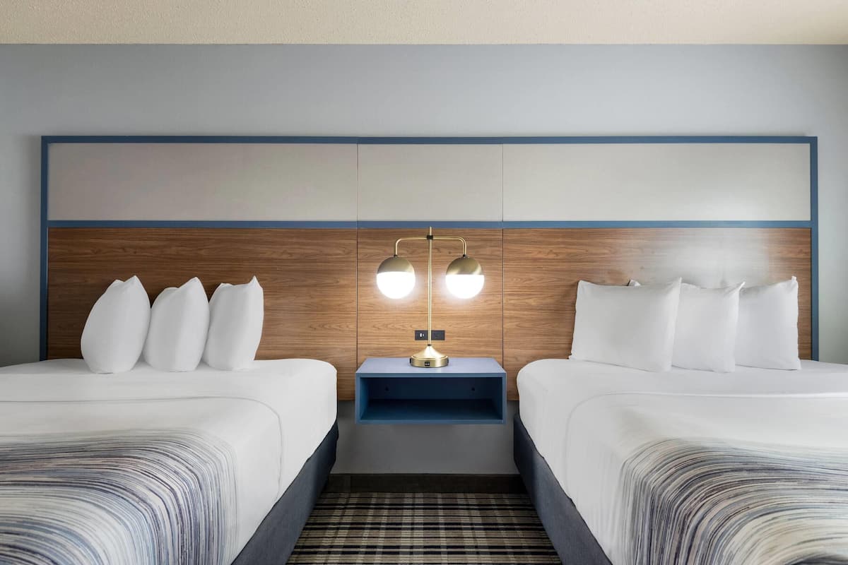 A hotel room with two beds, a nightstand with a lamp, and a wooden headboard.