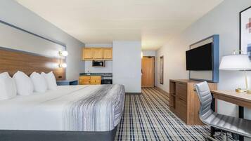 A hotel room with a large bed, a desk with a chair, a television, and a kitchenette.