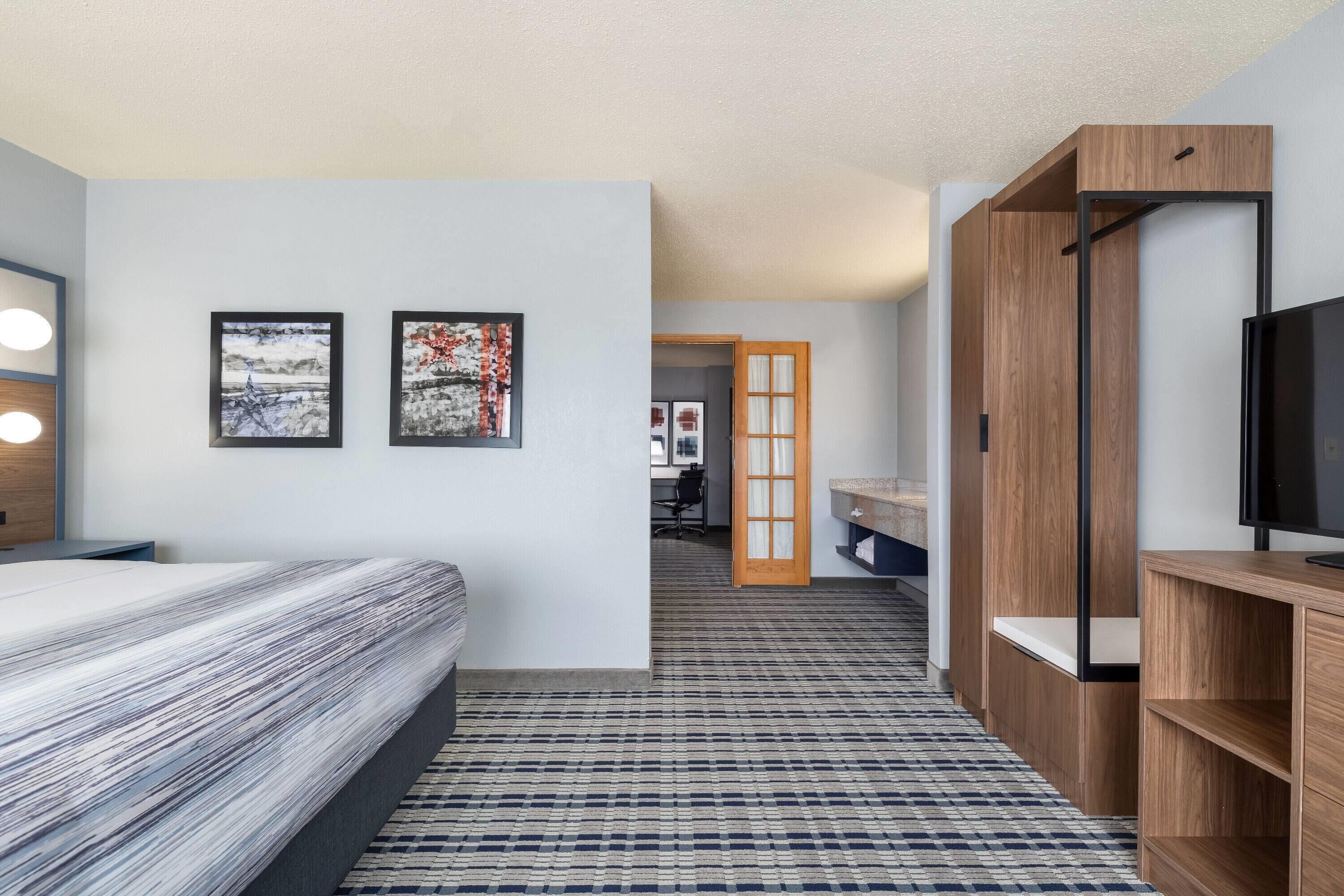 A hotel room with a bed, a TV, a desk, and a bathroom visible through an open door.