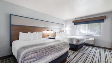 Une chambre d’hôtel avec un grand lit, un lit plus petit, une table de chevet avec une lampe, une fenêtre et un climatiseur fixé au mur.