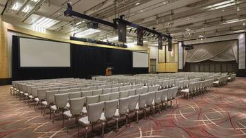A large conference room with rows of chairs, a stage with a projector, and a carpeted floor.