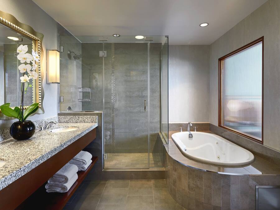 Un baño moderno con encimera de granito, un espejo grande, cabina de ducha y bañera independiente.