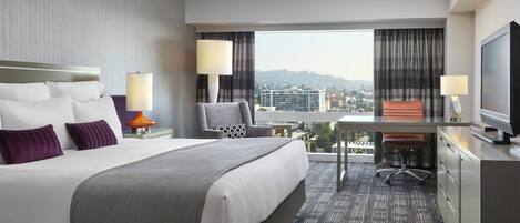 Habitación de hotel con una cama grande, un escritorio, una silla, un televisor y vistas a la ciudad.