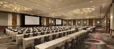 A large conference room with rows of tables and chairs, a projector screen, and a carpeted floor.