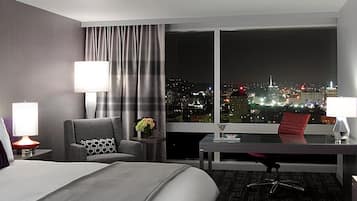 Une chambre d’hôtel avec un lit, un bureau, une chaise, une table et une vue sur le paysage urbain la nuit.