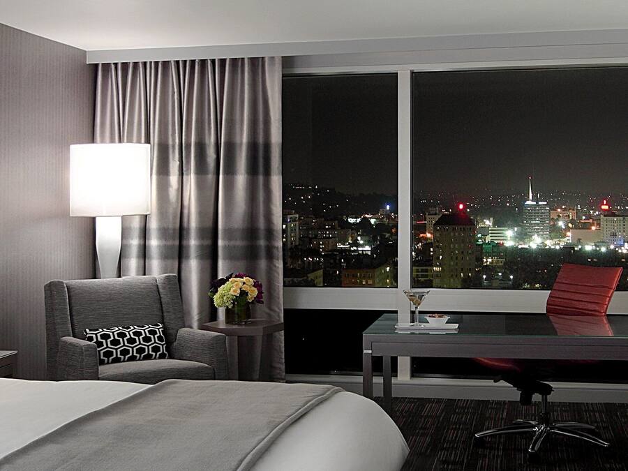 Une chambre d’hôtel avec un lit, un bureau, une chaise, une table et une vue sur le paysage urbain la nuit.