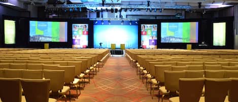 A conference room with rows of chairs facing a stage with a large screen displaying text.