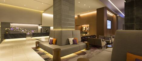 A modern lobby with a central seating area, a reception desk, and a bar.