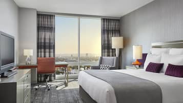 Habitación de hotel con una cama grande, dos sillas, un escritorio, televisión y vistas a la ciudad.
